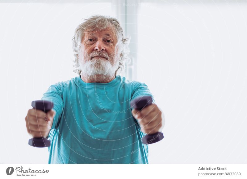 Cheerful elderly man exercising with dumbbells exercise smile morning home fitness training happy gymnastic male senior aged pensioner activewear activity