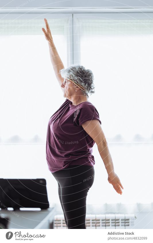 Senior woman exercising in morning exercise stretch home gymnastic arm raised training early fitness female elderly senior aged sunlit healthy lifestyle
