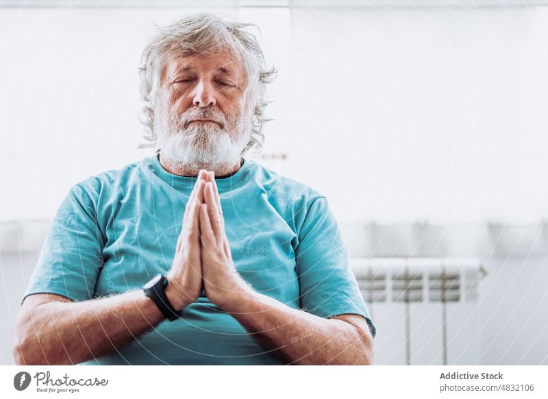 Relaxed aged man meditating in morning meditate home relax yoga session namaste practice calm male elderly senior retire pensioner hands clasped mindfulness zen