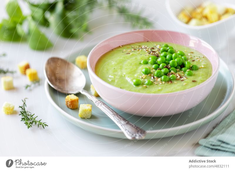 Healthy cream pea soup in a bowl green vegetable vegetarian puree healthy light diet bread cubes spoon garnish herb aromatic delicious recipe dinner lunch thyme
