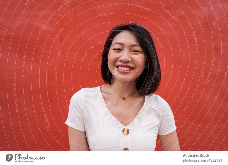 Delighted young ethnic woman smiling at camera against red wall smile cheerful self assured personality positive portrait happy charismatic glad optimist