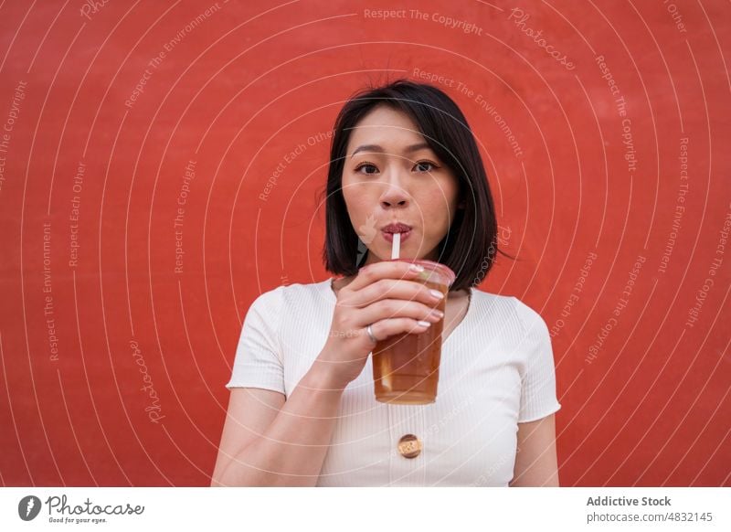 Young ethnic lady drinking takeaway refreshing beverage on street woman coffee refreshment portrait to go confident style straw female young asian brunette