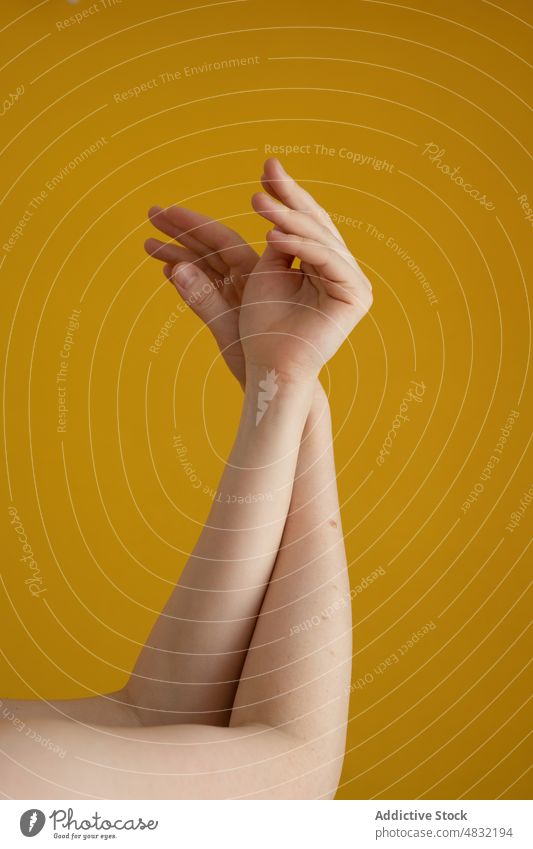 Crop unrecognizable lady holding hands against yellow background woman grace arms raised feminine tender gesture peaceful idyllic calm harmony mole female