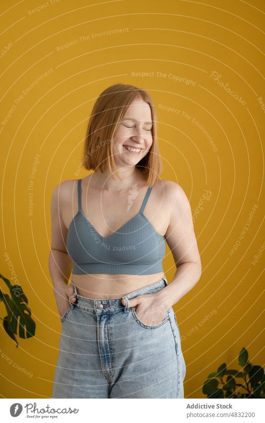 Positive young lady in bra smiling brightly with closed eyes woman smile eyes closed cheerful hand in pocket confident happy model positive portrait delight