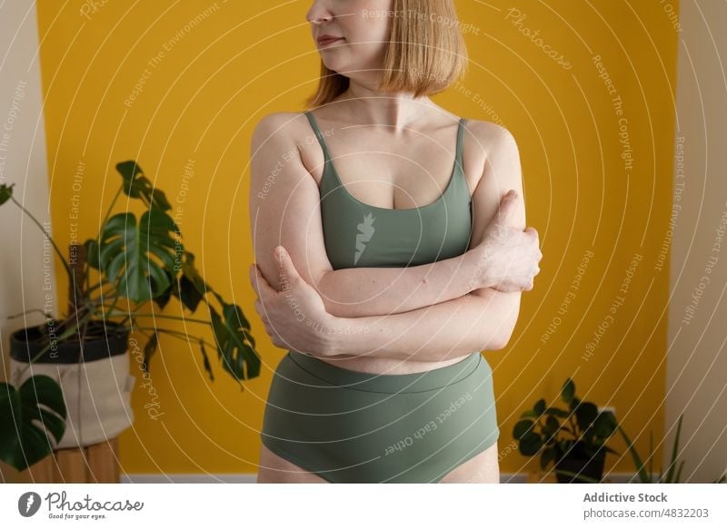 Anonymous curvy lady with arms crossed standing near yellow wall woman body positive plus size model figure natural personality confident feminine curve