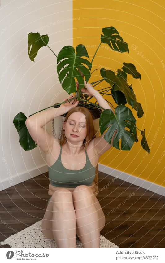 Calm lady with closed eyes sitting on floor and touching Swiss cheese plant woman eyes closed monstera deliciosa swiss cheese plant relax calm allure feminine