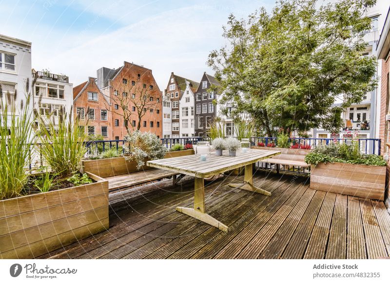 Wooden table on spacious terrace of residential building district city architecture veranda cozy plant decor neighborhood dwell multistory property estate