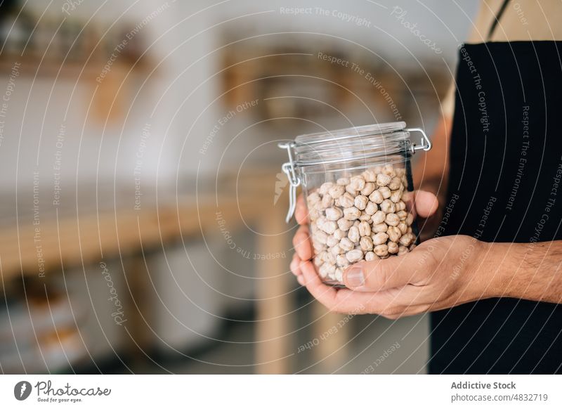 Shopkeeper holding glass jar with chickpeas shopkeeper anonymous store dry fill local seasoning customer ecological consume buyer purchase female shovel natural