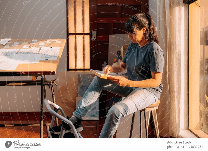 Woman drawing on white paper near window interior woman adult lifestyle creative studio workplace artistic pretty skill hobby paint casual painter female