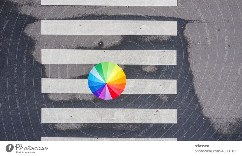 Top view of a rainbow umbrella on a pedestrian crosswalk top crossing color drone road city walking minimal background asphalt white rainy loneliness straight