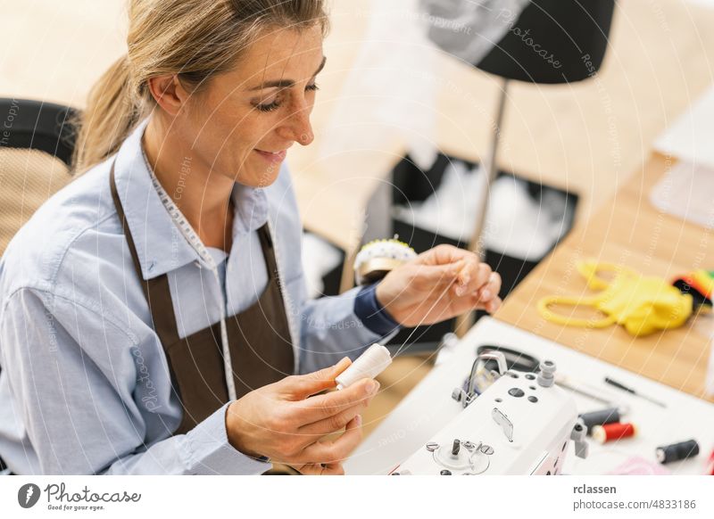Young dressmaker woman sews clothes on working table. Smiling seamstress and her hand close up in workshop. Focus on suture on table machine lace needle sewer