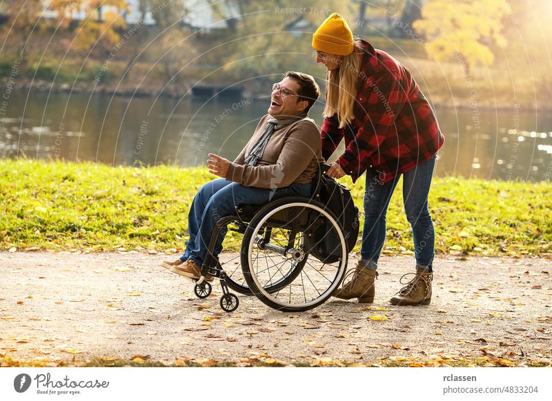 Woman and her friend in a wheelchair having stroll through the park at a river enjoying the autumn disability city couple friends germany girlfriend happy help