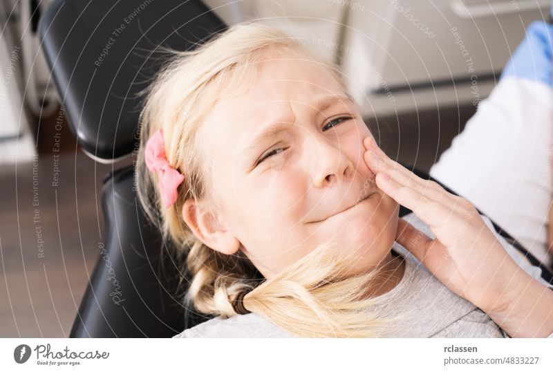 Little child at dentist office in comfortable chair touching mouth with hand with painful expression because of toothache or dental illness on teeth. Dentist concept image