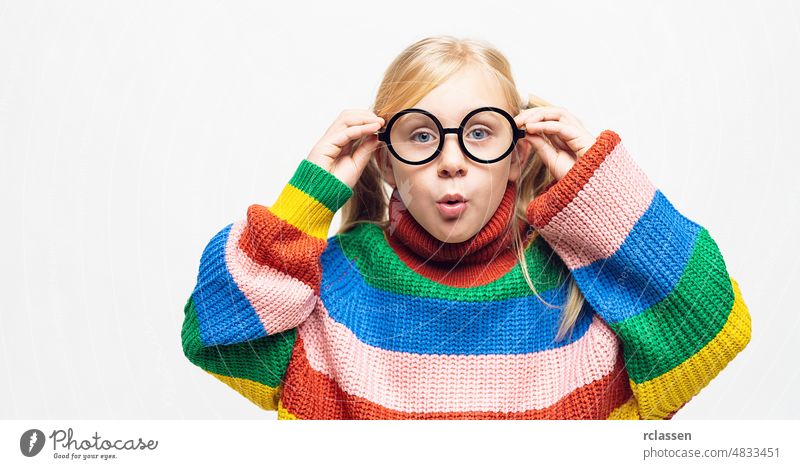 small girl is amazed and her hands touch eyeglasses wear rainbow style pullover and hispter glasses isolated on white background kid crazy fun cheerful