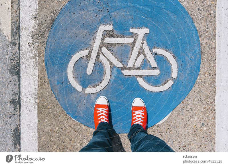 Man standing on bicycle zone sign on a asphalt city street in red sneakers, point of view perspective pov conceptual floor urban step blue ground legs adventure