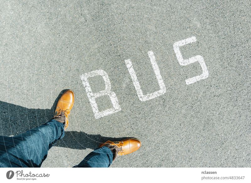 Man standing on grunge asphalt city street with white text bus, point of view perspective pov conceptual floor sign urban step copy space ground legs wait