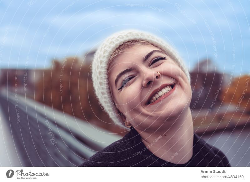 portrait of a young woman in a cap who is very happy smile lucky exterior outdoor bridge river autumn sky blue teen teenager casual caucasian female lifestyle