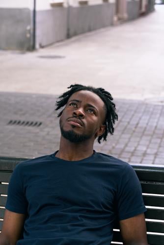 young man of color rests on a bench face faceup portrait  Alone   Casual   City   Outdoor   Spain   Street   Twenties   Trendy   Urban   Young  Casual Clothing