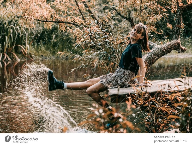 Young woman sitting on wooden bridge spraying water with boots Bridge Water Boots Wet Summer Exterior shot Colour photo Feminine Joy stylish cheerful