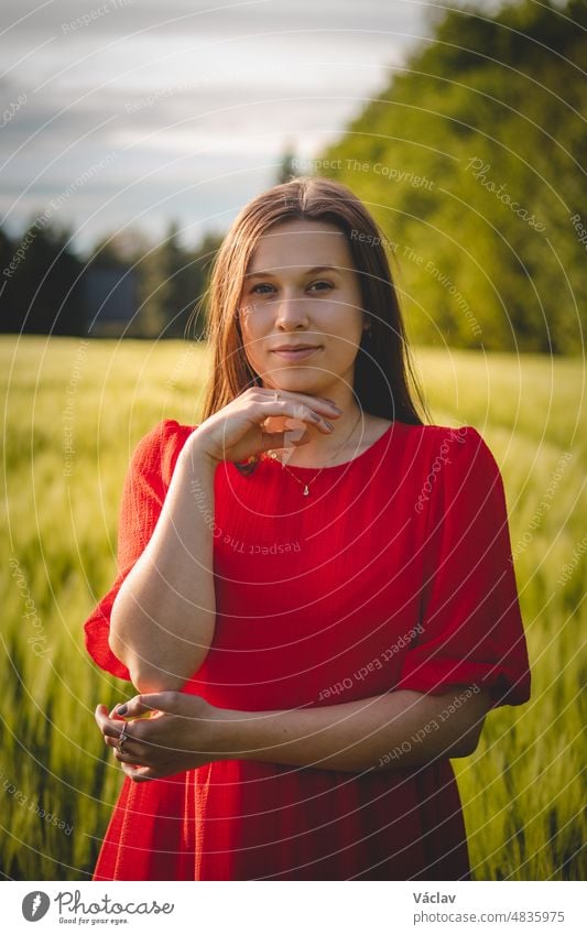 Breathtaking candid portrait of a brunette aged 20-24 in a loose red dress in a cornfield, smiling naturally. Fashion vintage style. Natural beauty of a brown haired European woman