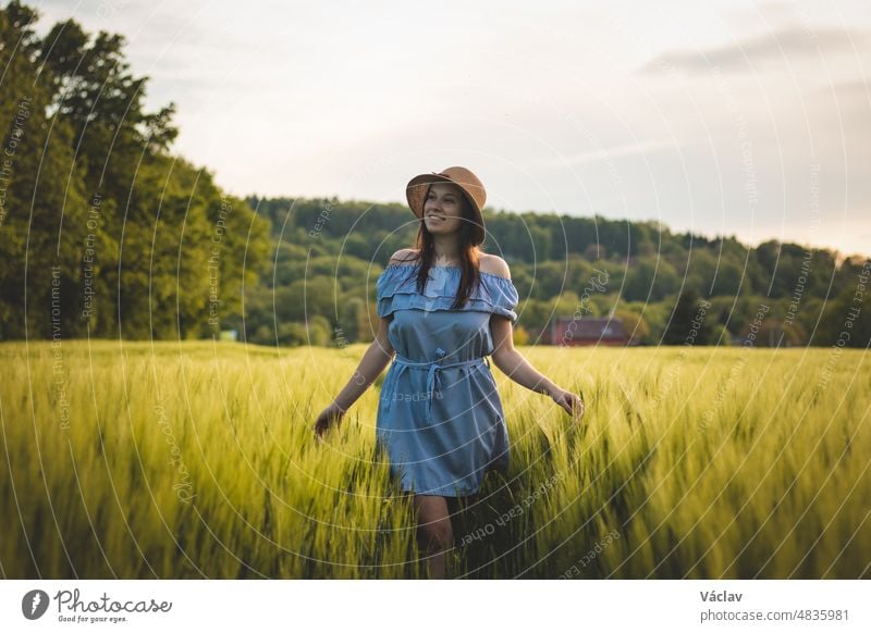 Breathtaking candid portrait of a brunette aged 20-24 walks in a beautiful blue dress and hat in a cornfield, smiling naturally. Fashion vintage style. Natural beauty of a brown haired European woman