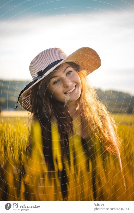 Candid portrait of a young woman from the Czech Republic sitting in the middle of a field at sunset, enjoying the remnants of the rays in a flowered dress. Real smile