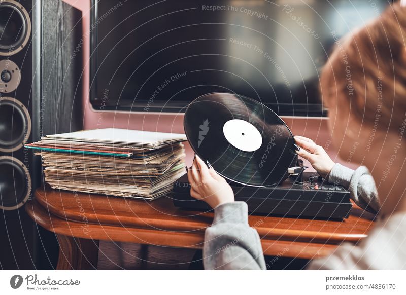 Young woman listening to music from vinyl record player. Retro and vintage music style. Girl holding analog record album. Female enjoying music from old record collection