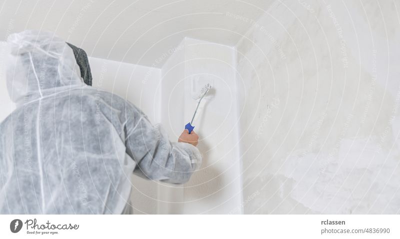 painter stands with paint roller on a ladder to paint the corner of a room window with white color. do it yourself concept image arm close up construction decor