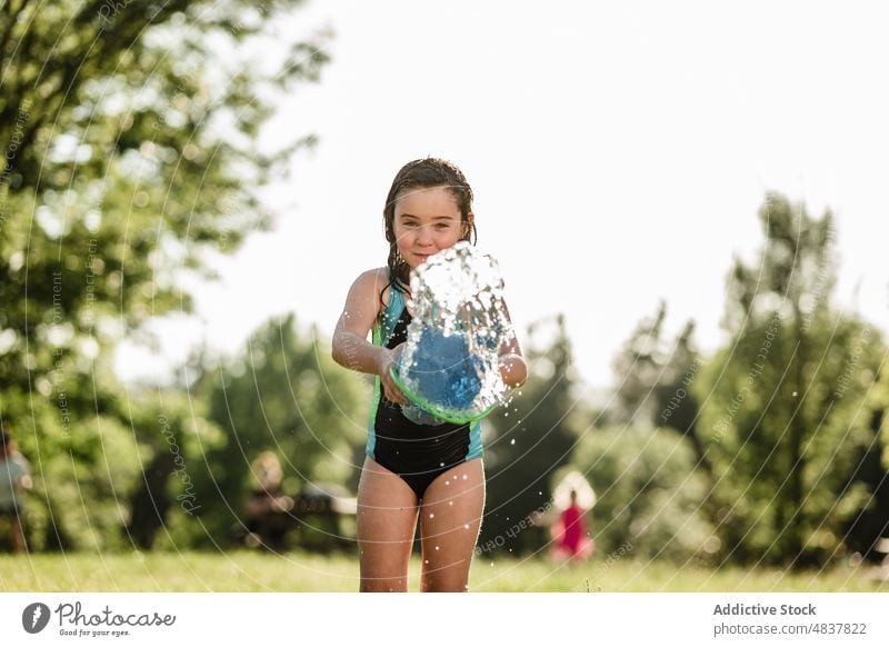 Little girl playing with bucket in park summer female throwing water towards camera herself holiday childhood kid lifestyle joy season young enjoy garden