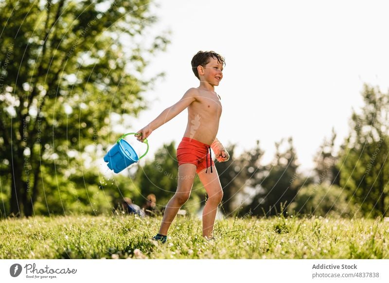 Happy boy playing with water shirtless childhood summer park kid lawn happy nature activity athlete carefree naked torso little cheerful meadow together sun