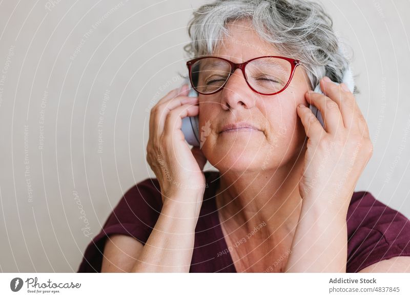 Satisfied senior lady listening to music in headphones with closed eyes woman eyes closed meloman enjoy song audio content positive favorite melody female
