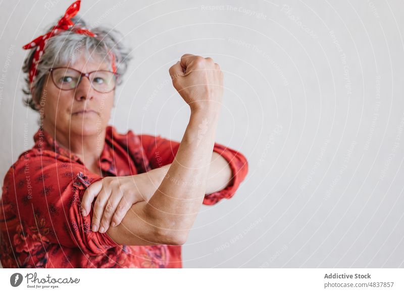 Serious elderly feminist showing muscles and looking at camera woman bicep pin up concentrate style pretend power strong demonstrate muscular female senior
