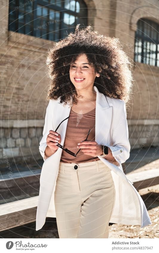 Hispanic businesswoman holding sunglasses on street walk urban style confident entrepreneur suit female hispanic ethnic shabby building trendy weathered