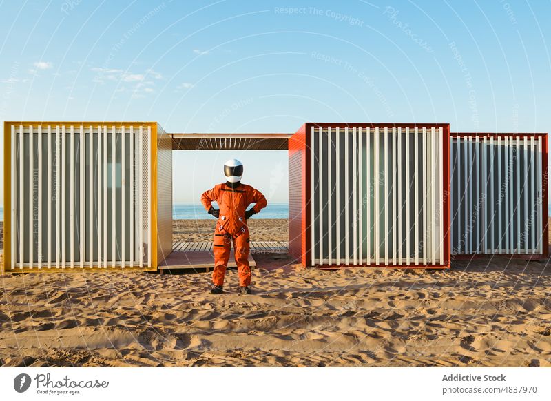 Unrecognizable spaceman standing on alien beach astronaut sea admire building futuristic concept explore spacesuit sand geometry blue sky cosmonaut