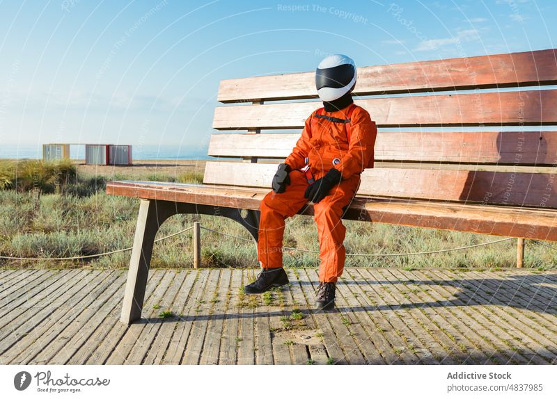 Spaceman sitting on giant bench astronaut beach explore expedition alien concept small spacesuit helmet cosmonaut protect spaceman planet futuristic mission