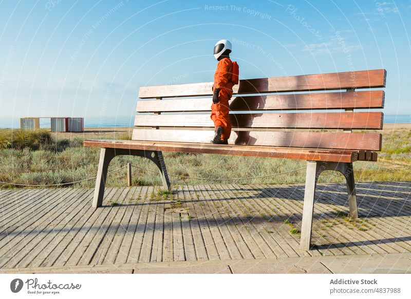 Spaceman standing on giant bench astronaut beach explore expedition alien concept small spacesuit helmet cosmonaut protect spaceman planet futuristic mission