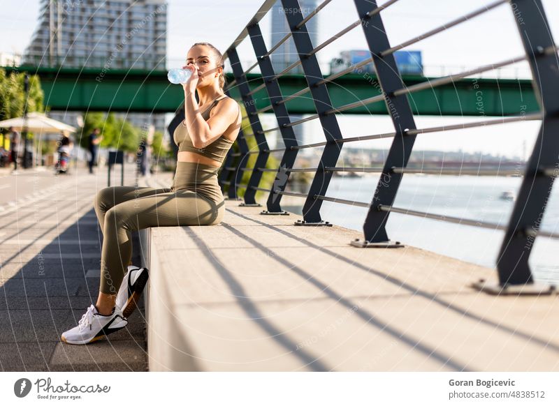 Pretty young woman with earphones takes a break after running in urban area athlete athletic arabic exercise female fit fitness bottle drink healthy jogger