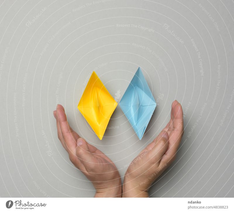 Two yellow-blue paper boats in female palms on a gray background support concept ukraine hand feminine sympathy unity symbol freedom national peace ukrainian