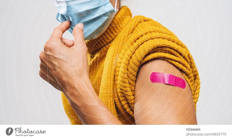 Vaccinated Woman Showing Arm With Pnk Plaster Bandage Protection would like to takes off Face Mask, After Covid-19 Vaccine Injection Posing Gray Background, Coronavirus Vaccination, copy space