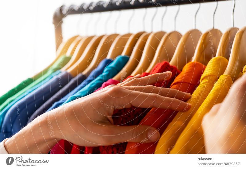 Fashion clothes hanging on clothing rack - bright colorful rainbow selection of clothes closet. Woman choose outfits on hangers in store closet. LGBT colors