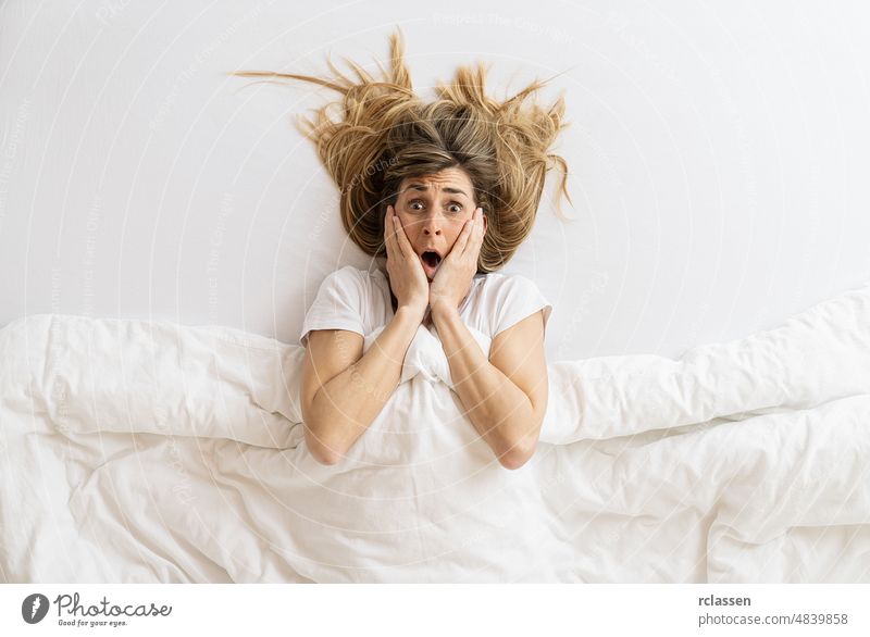 Top view of a shocked woman that looks at camera while lying in bed under blanket, copyspace for your individual text. top funny sex awake female happy