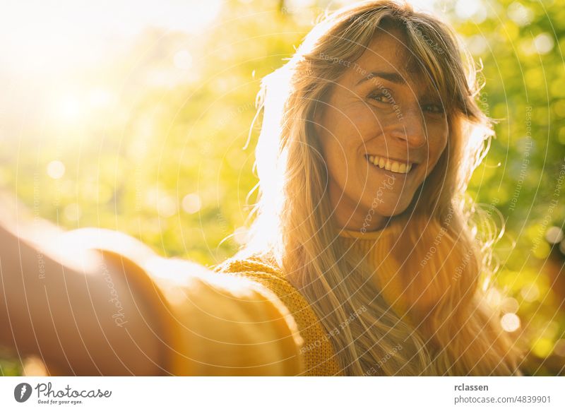Close up portrait of beautiful woman with long blond hair, taking selfie with smartühone on sunny day in the Nature adult attractive backlit influencer brunette