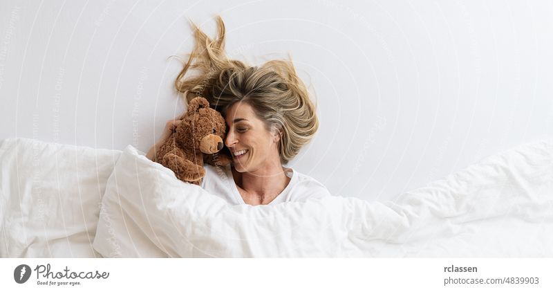 woman that cuddles with her teddy bear sleeping on white bed and lying under blanket, Top view,  copyspace for your individual text. top above smile friend