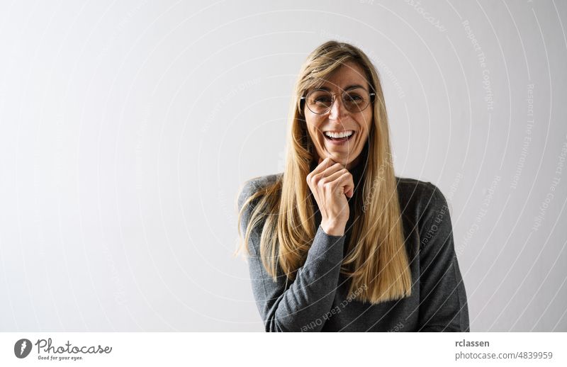 friendly woman with a lovely sense of humour standing in a white room hold hand under chin, wall with copy space at home and looks to the the camera happy smile
