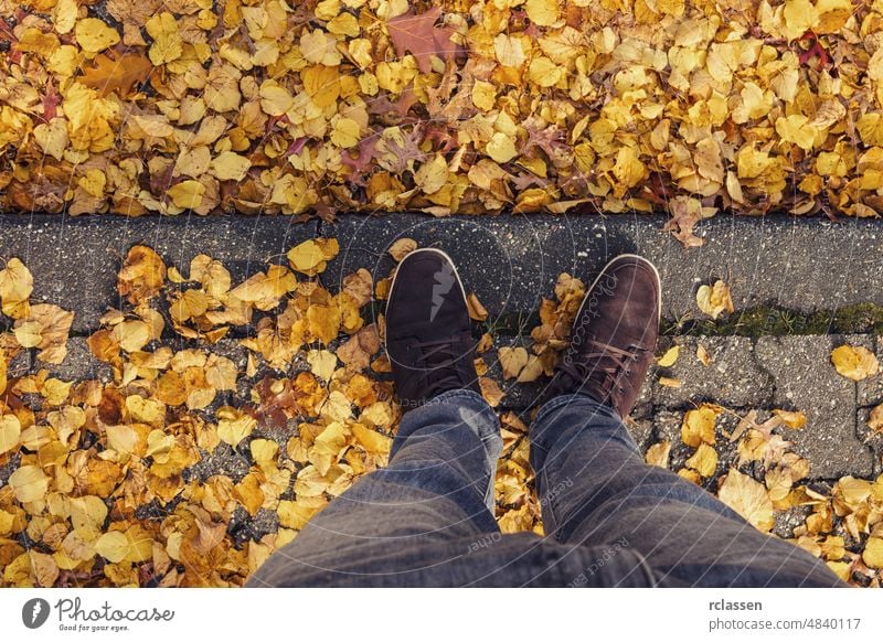 Young man stands in at a curbstone with foliage leafs at autumn on the streets, personal pespective from above. pov people lifestyle point view way caucasian