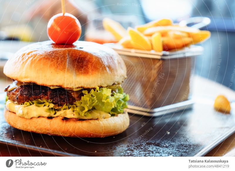 A selective focus on a fresh burger with a patty, cherry tomato and lettuce. French fries in the background hamburger snack sandwich meat grilled food fast meal