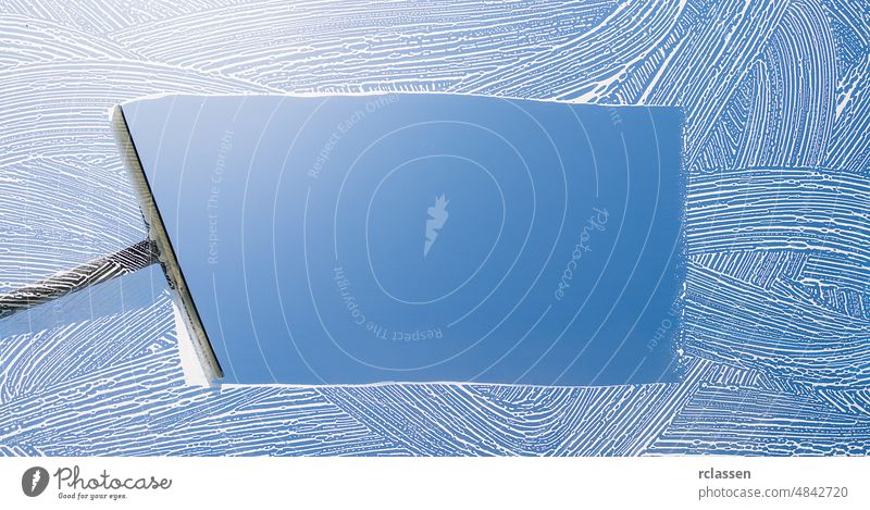 Rubber squeegee cleans a soaped window and clears a stripe of blue sky, concept for tranparency or spring cleaning, with copyspace for your individual text.