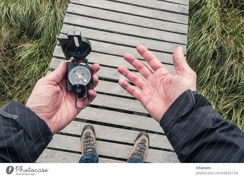 Man hold a compass and searching direction the direction on a wooden boardwalk, point of view. man holding pov orientation hand people lifestyle orienteering