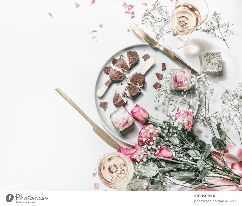 Aesthetic summer table setting with ice cream popsicles , flowers bouquet, champagne glasses and golden cutlery at white background. aesthetic top view