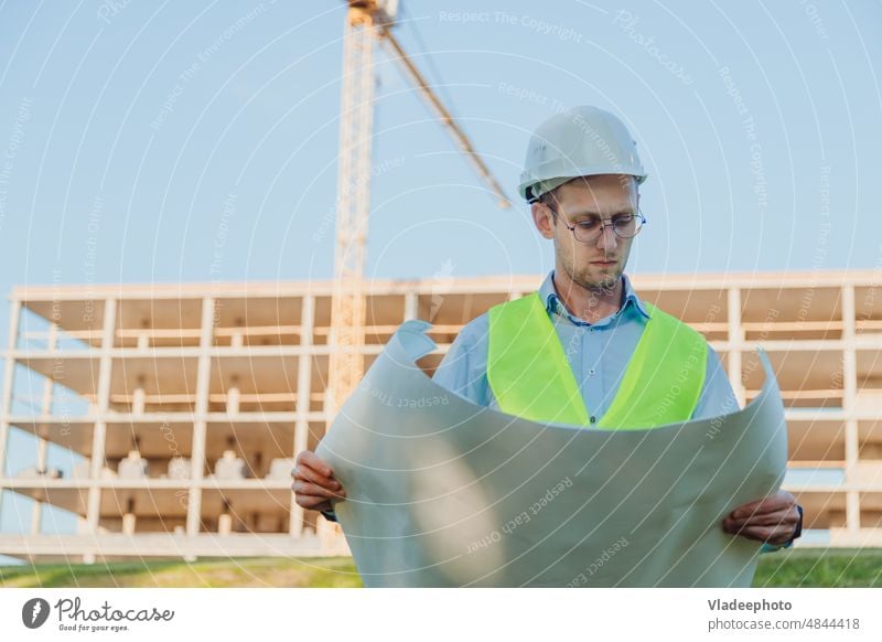 Male civil engineer in helmet and vest checking architectural drawing at construction site man blueprint project foreman contractor architecture worker